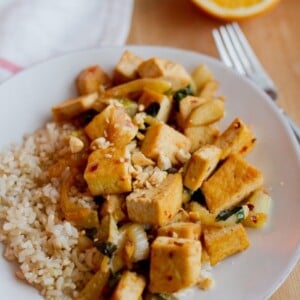 Orange tofu stir-fried with fennel and served over brown rice on the white plate.