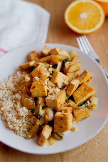 Orange tofu stir-fried with fennel and served over brown rice on the white plate.