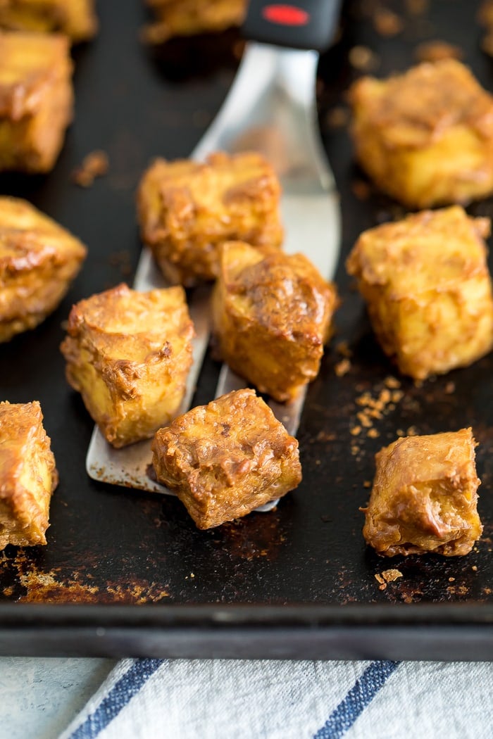 Sheet pan with crispy baked peanut tofu and a spatula lifting tofu off of the sheet.