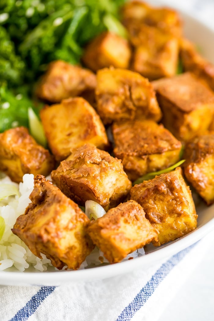 Bowl with kale topped with sesame seeds, crispy baked peanut tofu, and rice topped with scallions.