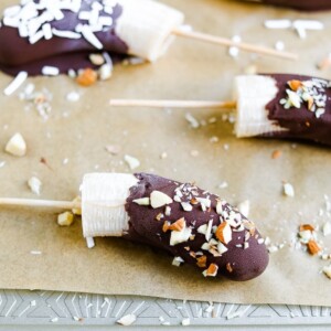 Chocolate covered bananas on parchment paper lined cookie sheet and sprinkled with almonds and coconut.