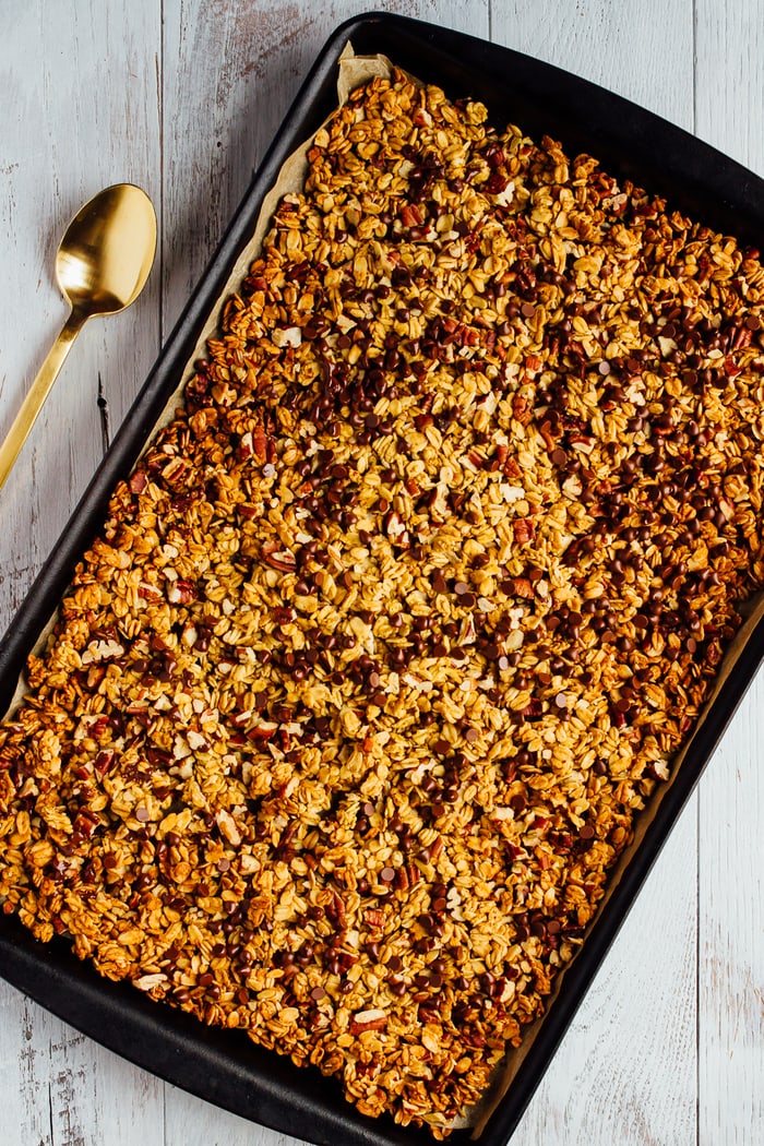 Chocolate Pecan Pumpkin Granola on a baking sheet with a spoon to the side.