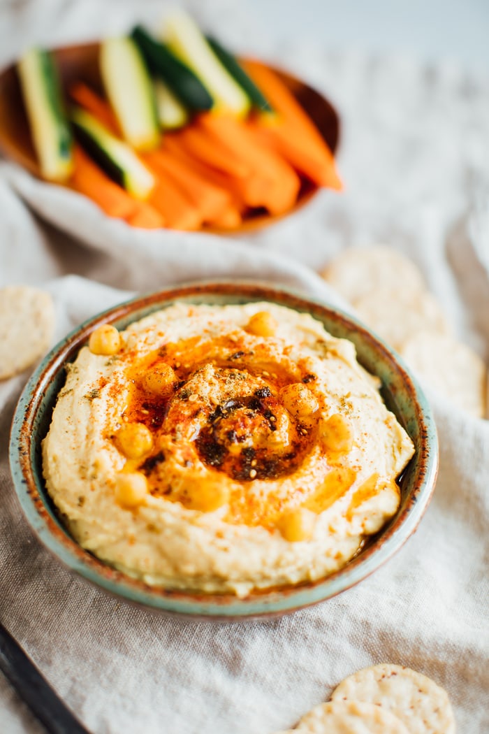 Bowl of hummus topped with spices and chickens next to a bowl of chopped raw veggies.