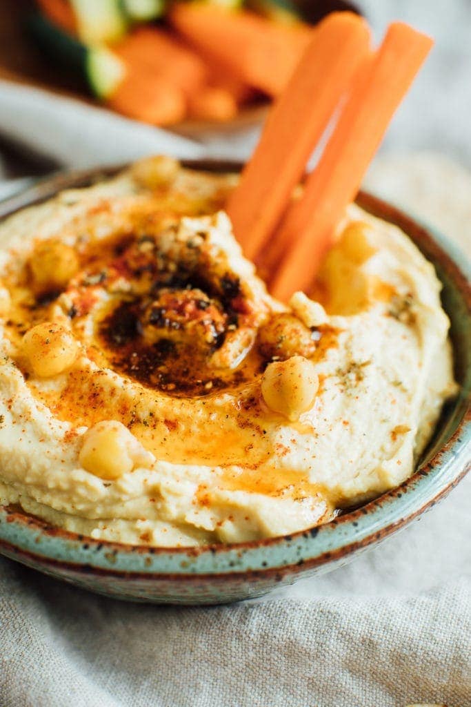 creamy hummus topped with chickpeas, olive oil, spices and dipped with carrot sticks.