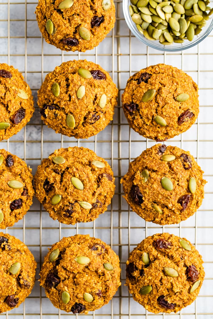 Pumpkin bran muffins on a cooling rack next to a bowl of pumpkin seeds.