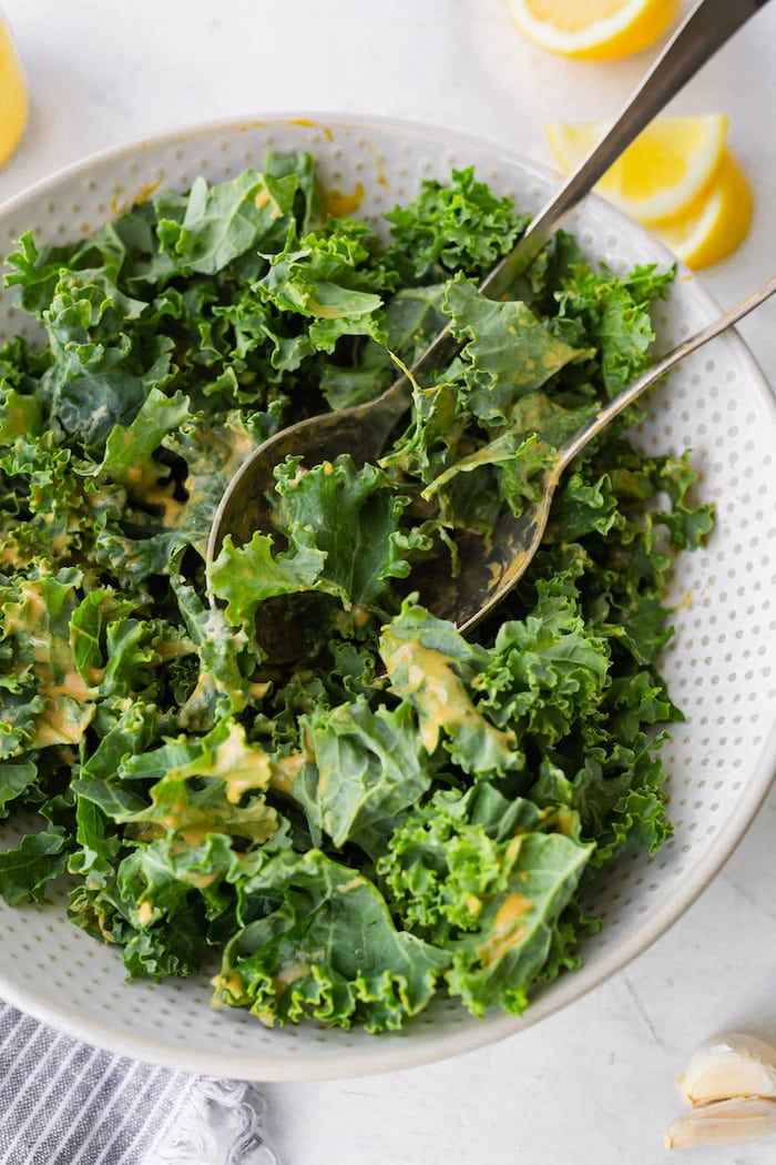 Raw kale in a white bowl with tahini dressing drizzled over.