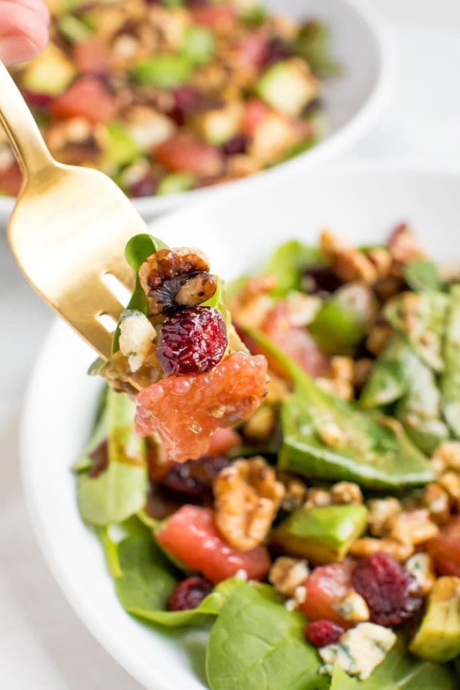 A fork holding up a bite of salad over a bowl.