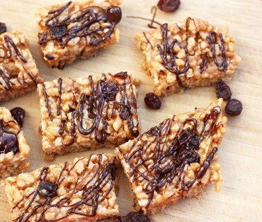 Healthy brown rice krispy treats on a wooden cutting board with chocolate drizzle.