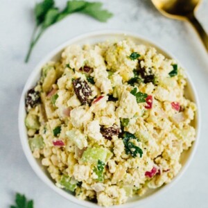 Overhead shot of Vegan Chicken Salad made with tofu, celery, almonds and raisins in a white bowl on white countertop.