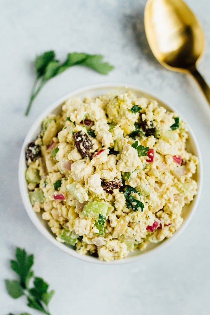 Overhead shot of Vegan Chicken Salad made with tofu, celery, almonds and raisins in a white bowl on white countertop.