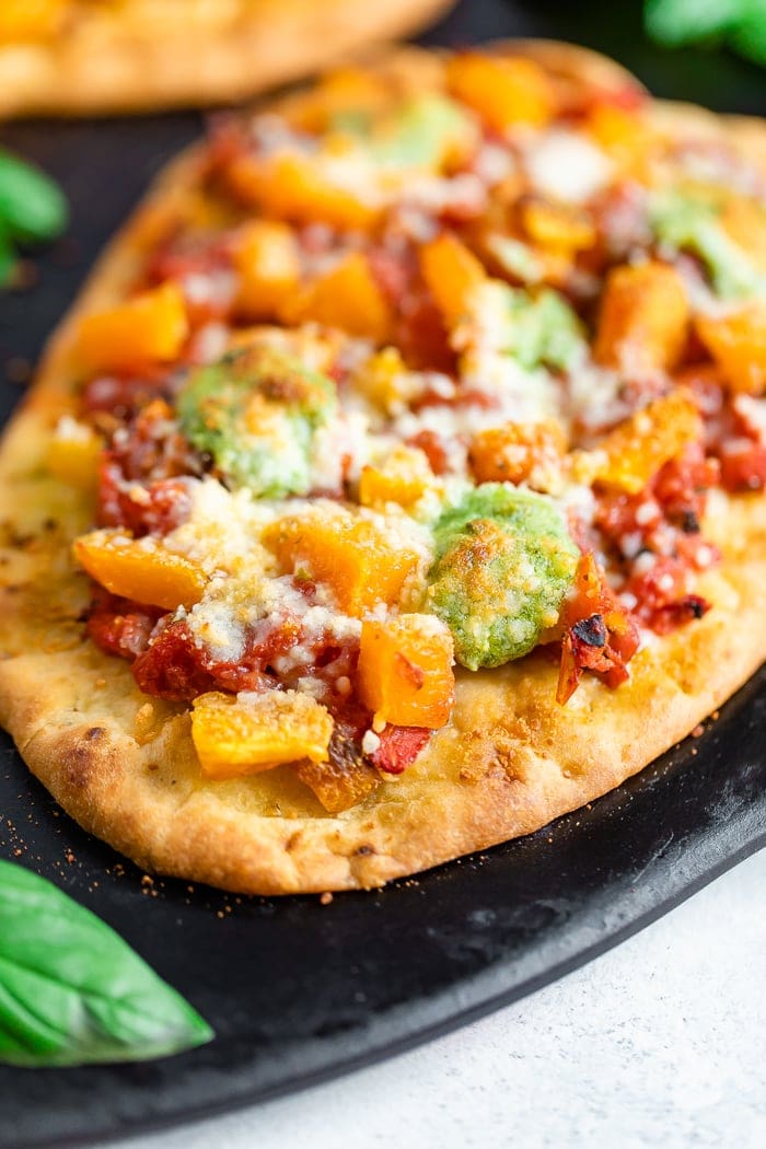 Naan pizza topped with tomatoes, butternut squash, pesto, and cheese.