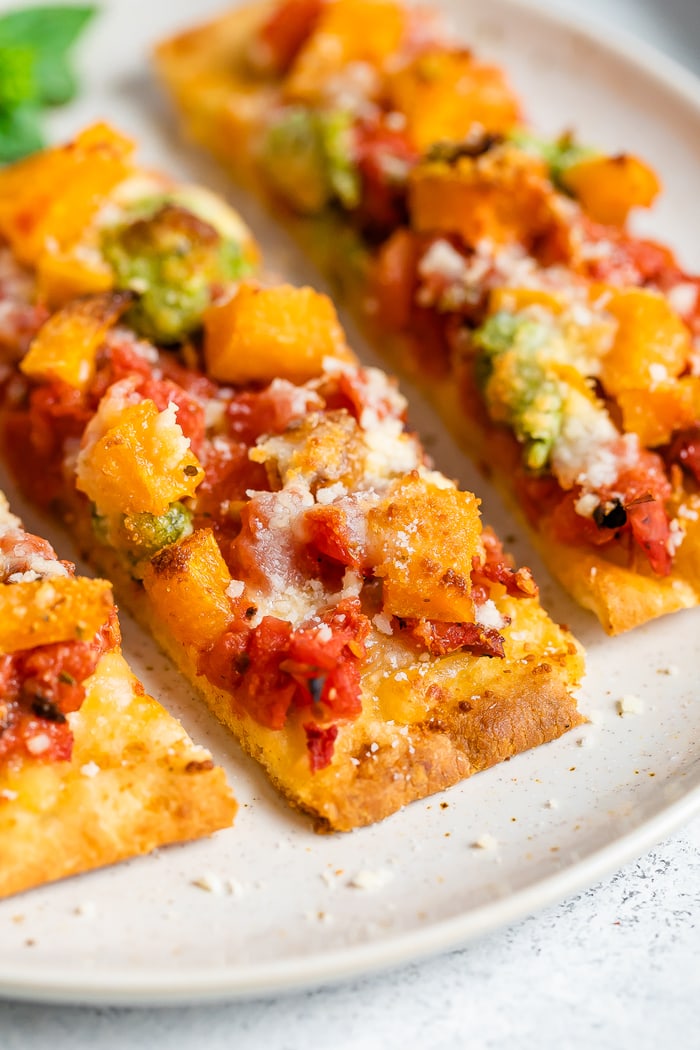 Slices of naan pizza topped with cheese, tomatoes, butternut squash, and pesto.