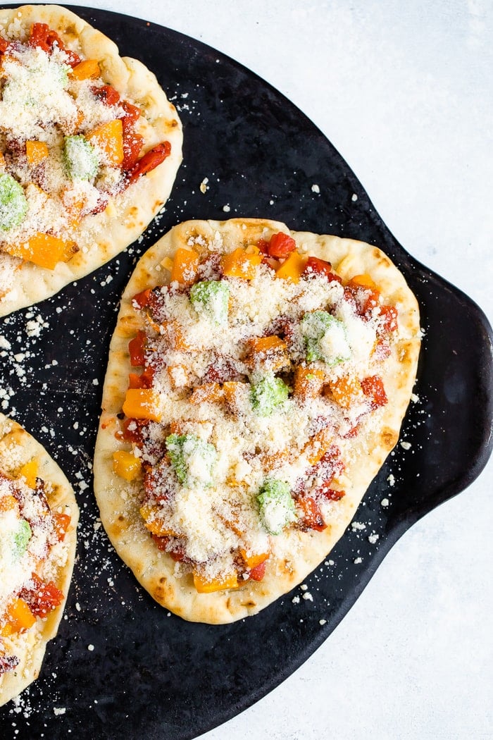 Unbaked naan pizza on a pizza stone with tomatoes, butternut squash, pesto, and cheese.