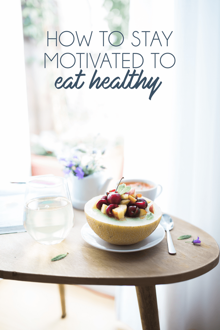 Wood table with fruit bow, water, and flowers. 'How to stay motivated to eat healthy' in text overlaying the image. 