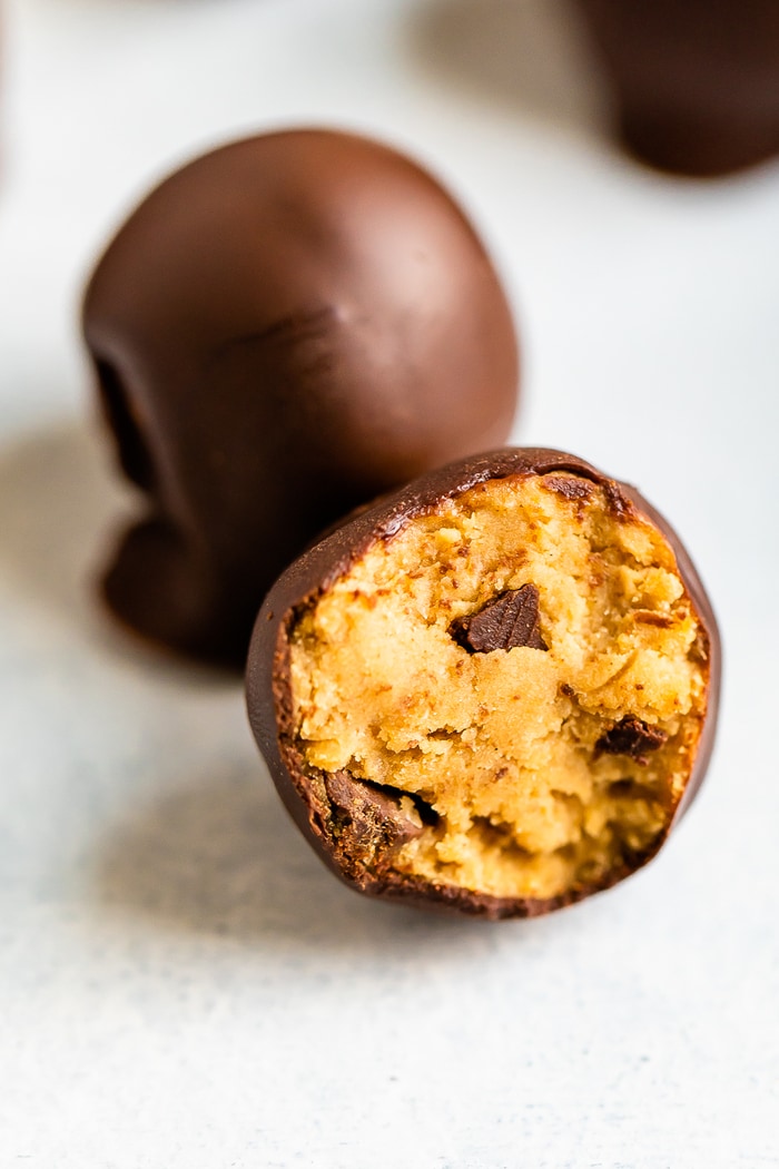 Two chocolate covered cookies dough bites. One has a bite out of it.