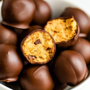 Bowl full of chocolate covered healthy cookie dough bites. One has a bite taken out of it.