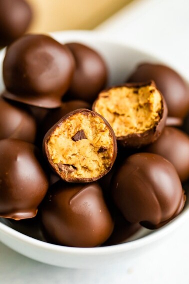 Bowl full of chocolate covered healthy cookie dough bites. One has a bite taken out of it.