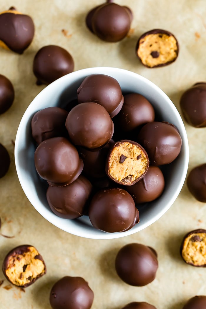 Bowl full of chocolate covered healthy cookie dough bites. Cookie dough bites are around the bowl as well and some have bites taken out of them.