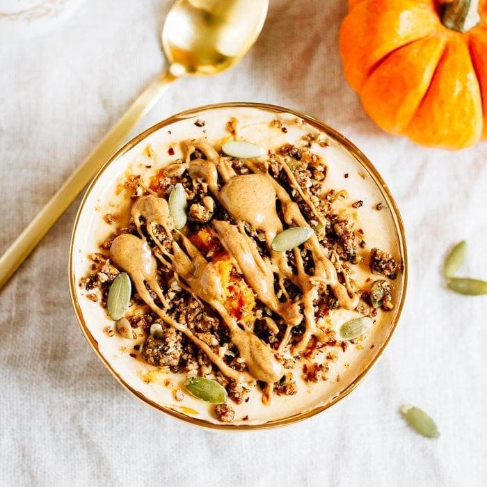 Bowl filled with yogurt and pumpkin and topped with seeds, granola and almond butter. Spoon and pumpkin off to the side.