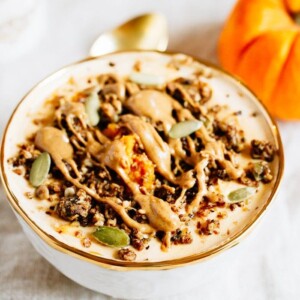 Bowl filled with yogurt and pumpkin and topped with seeds, granola and almond butter. Spoon and pumpkin off to the side.