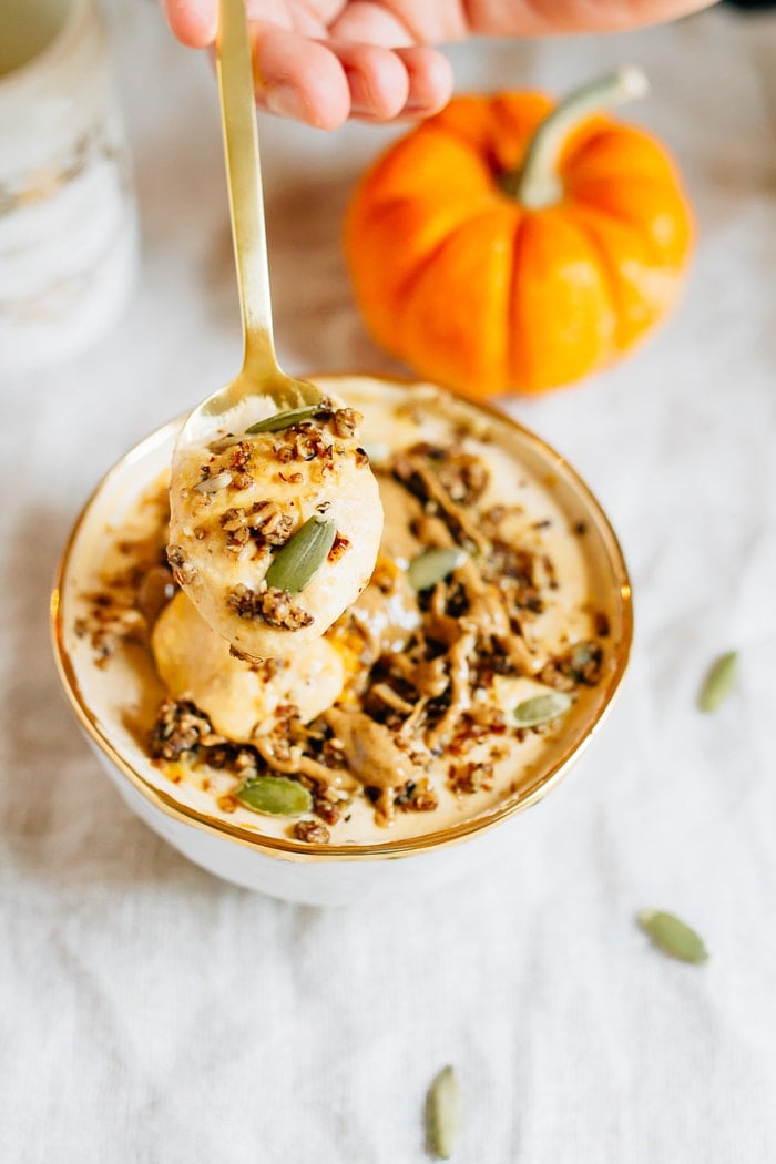 Bowl filled with yogurt and pumpkin and topped with seeds, granola and almond butter. Spoon in bowl with yogurt and pumpkin off to the side.