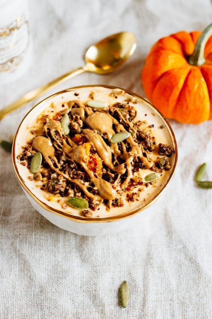 Bowl filled with yogurt and pumpkin and topped with seeds, granola and almond butter. Spoon and pumpkin off to the side.