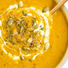 Bowl of healthy vegan curried pumpkin soup topped with pumpkin seeds and spices.