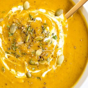 Bowl of healthy vegan curried pumpkin soup topped with pumpkin seeds and spices.