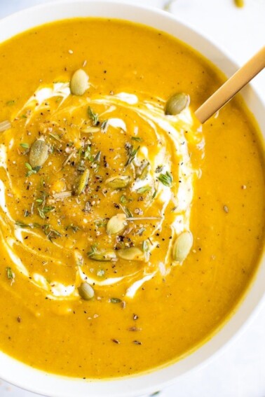 Bowl of healthy vegan curried pumpkin soup topped with pumpkin seeds and spices.