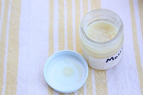 Jar of homemade face cream on a white and yellow striped towel. 