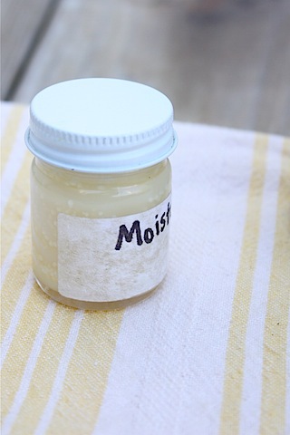 Jar of homemade face cream sitting on a white and yellow striped towel. 