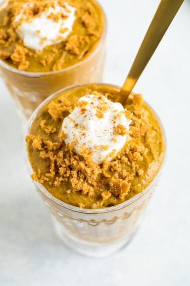 Two glasses of pumpkin chia mousse topped with greek yogurt and graham cracker crumbs.