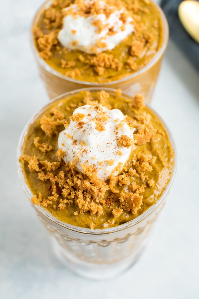 Two glasses of pumpkin chia mousse topped with greek yogurt and graham cracker crumbs.