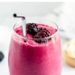 Glass of a blackberry smoothie topped with two berries and a straw.