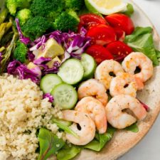 A huge plate with quinoa, greens, shrimp, cucumber, purple cabbage, tomatoes, broccoli, lemon, and asparagus