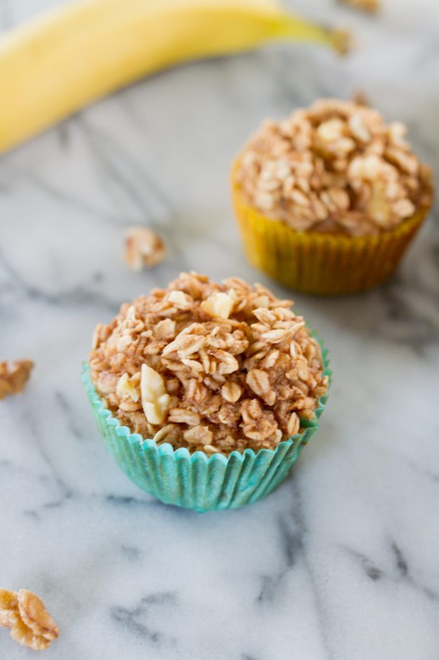 Two baked banana oatmeal cups in a cupcake liner, next to a banana.