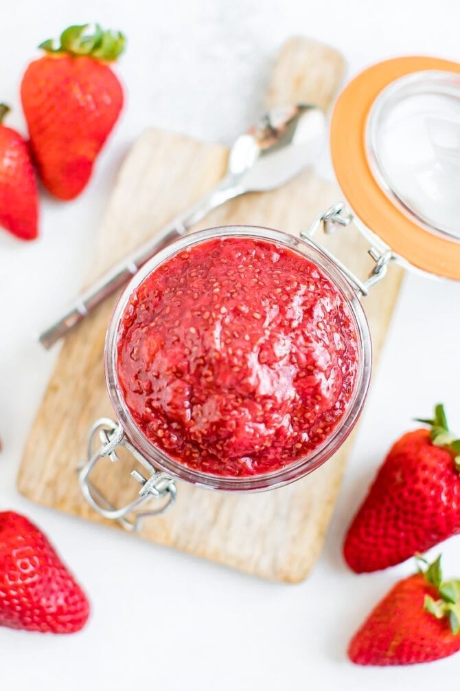 Close-up overhead shot of strawberry chia jam in a glass jar with fresh strawberries around the outside. 