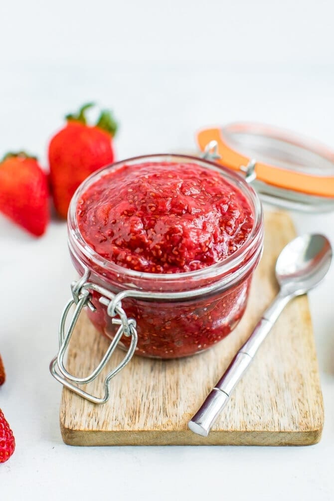 Strawberry chia jam in a glass jar with a silver spoon on the right. 