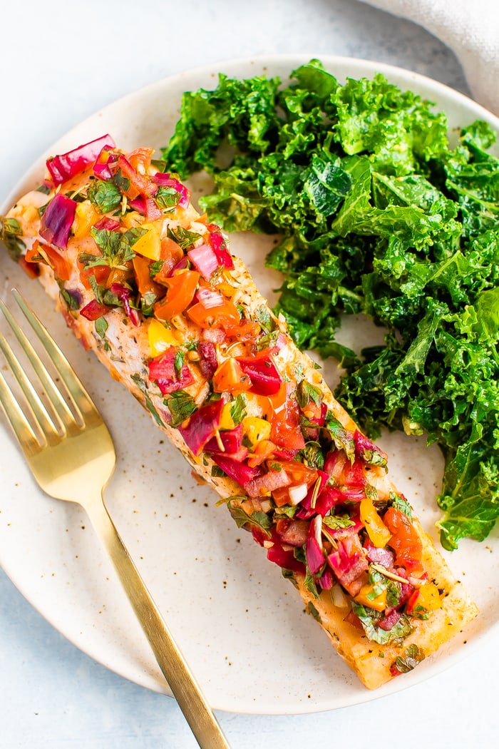 A plate with some greens and baked salmon with herbs and lime served with a golden fork.