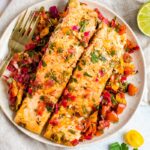 Overhead shot of baked salmon with herbs and lime on a white plate with a golden fork.