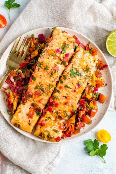 Overhead shot of baked salmon with herbs and lime on a white plate with a golden fork.