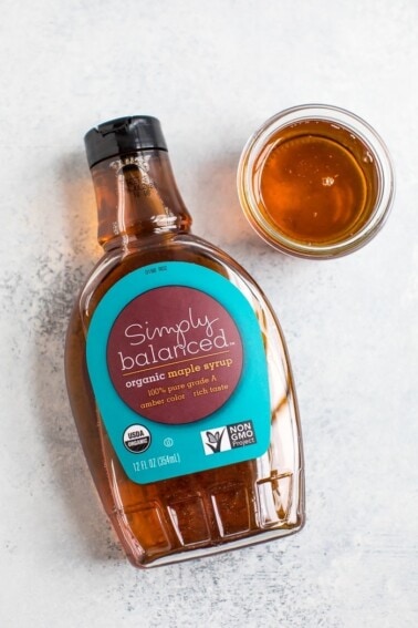Bottle of Simply Balanced maple syrup laying down on a counter. A small glass bowl with maple syrup poured into it is on the side of the bottle.