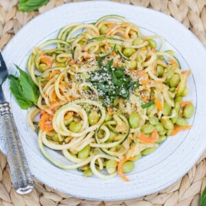 zucchini noodle pad Thai, with edamame, topped with chopped fresh basil leaves, on a white plate. A silver fork is sitting on the plate.