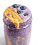 Blueberry smoothie with peanut butter drizzle in a jar. Blueberries are sprinkled on top.