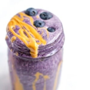 Blueberry smoothie with peanut butter drizzle in a jar. Blueberries are sprinkled on top.