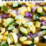 Roasted, chopped summer squash, zucchini, and red onion on a sheet with spices and pepper sprinkled on them.