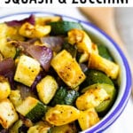 Bowl of roasted summer squash, zucchini, and red onion with pepper and seasoning. A wooden spoon is beside the bowl.