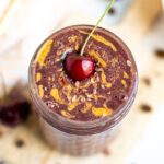 Mocha Cherry Smoothie in a glass mason jar topped with cacao nibs, a swirl of almond butter, and a cherry with a stem.