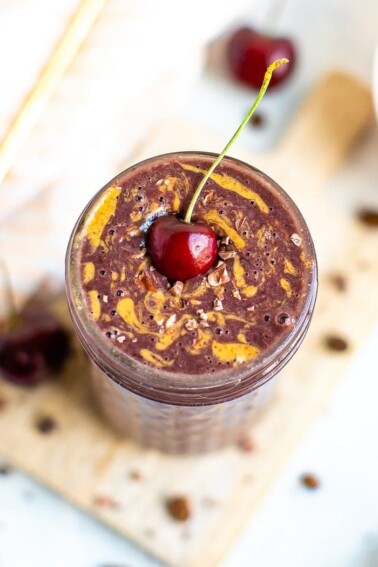 Mocha Cherry Smoothie in a glass mason jar topped with cacao nibs, a swirl of almond butter, and a cherry with a stem.