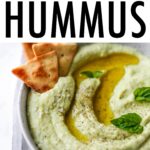 Bowl of lima bean hummus garnished with olive oil, pepper and basil and served with cucumbers, carrots and crackers.